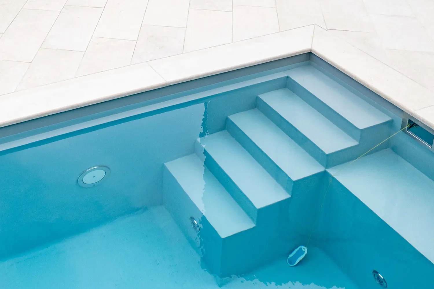Detailaufnahme einer breiten Pooltreppe mit heller Naturstein-Umrandung in klarem türkisfarbenem Wasser
